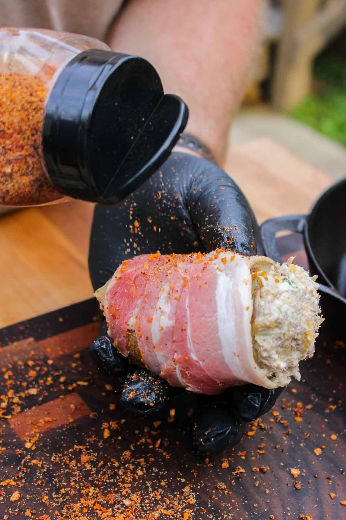 a bacon wrapped potato being seasoned with bbq seasoning