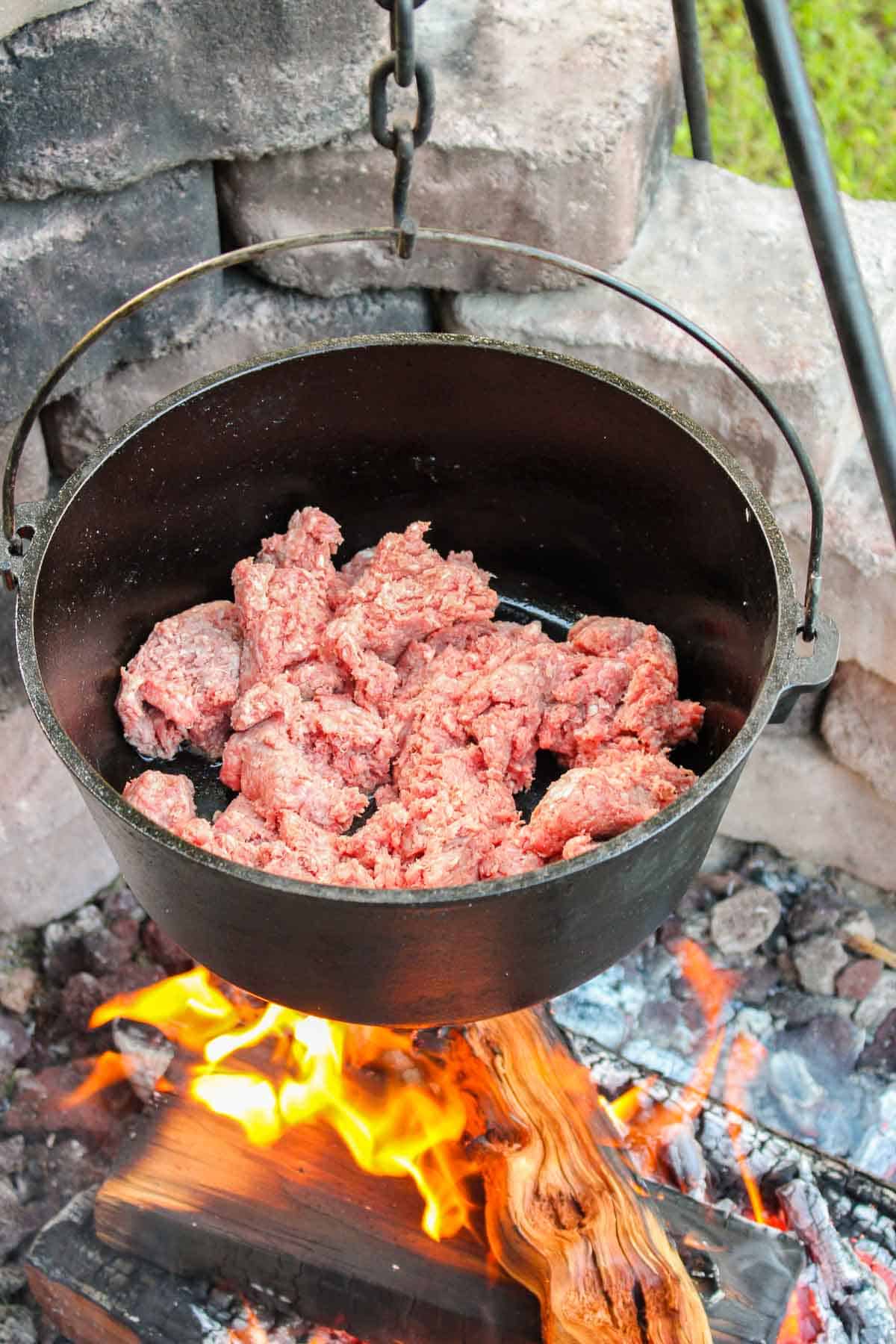 uncooked ground beef in a pot over a fire