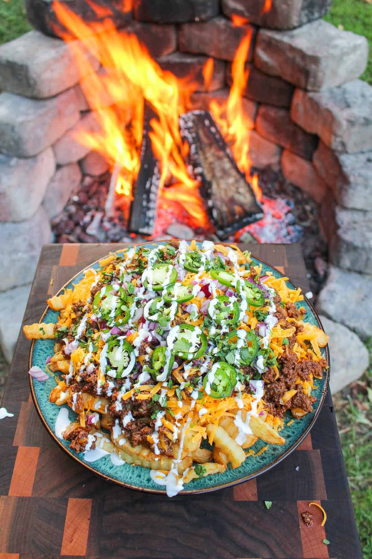 overhead of a plate of chili cheese fries next to a fire