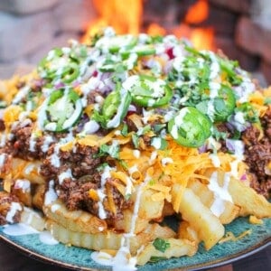a plate of loaded chili cheese fries set next to a fire