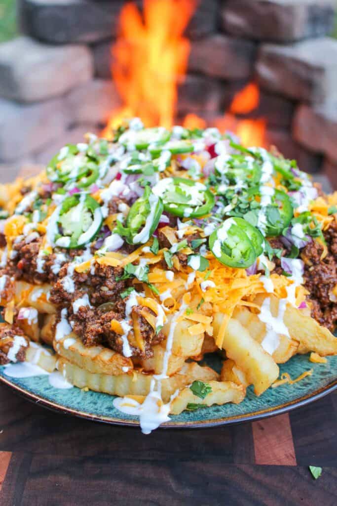 a plate of loaded chili cheese fries set next to a fire