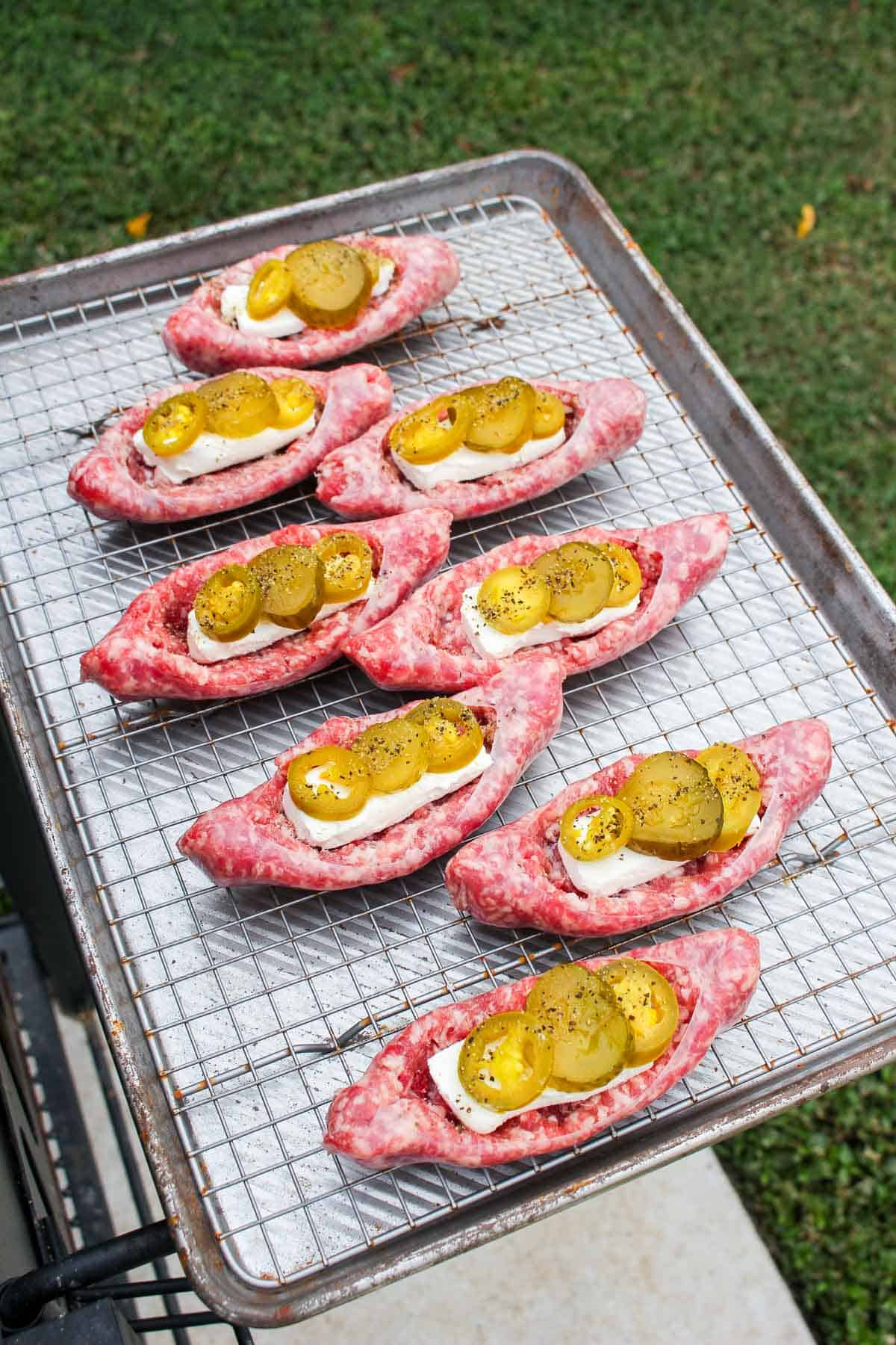 uncooked boat shaped sausage topped with cream cheese, pickles, and jalapeños on a baking sheet