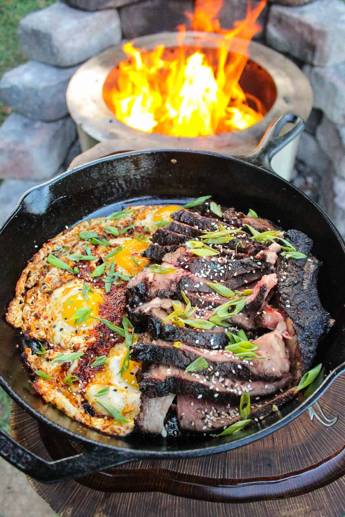 a skillet filled with steak and chili oil eggs by a fire