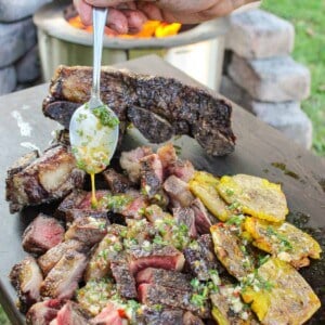 steak and smashed potatoes being drizzled with a spoonful of chimichurri butter