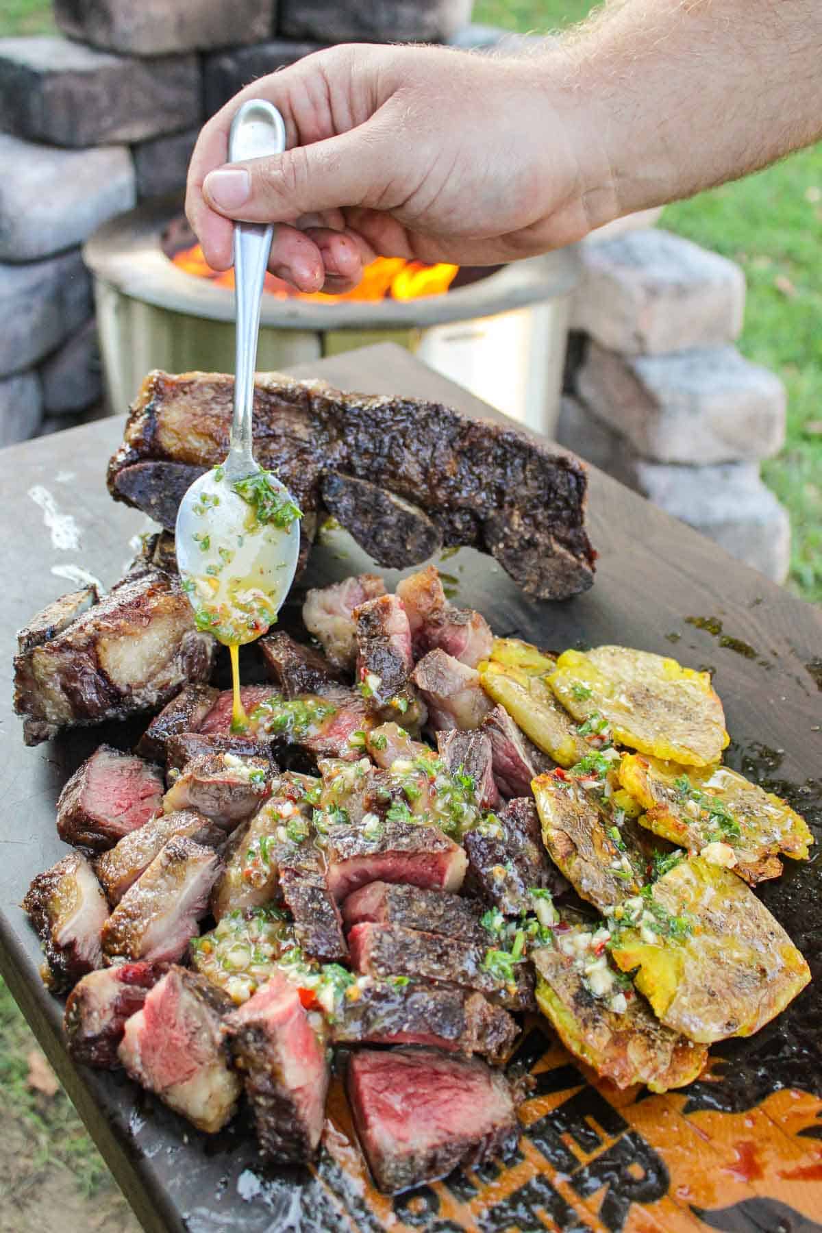 grilled beef short ribs and smashed potatoes being drizzled with a spoonful of chimichurri butter