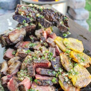 closeup of sliced steak topped with chimichurri butter next to smashed potatoes on a cutting board