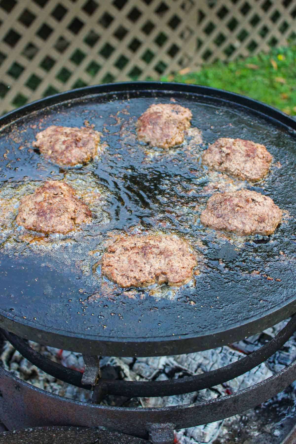 The burger patties cooking on the skillet. 