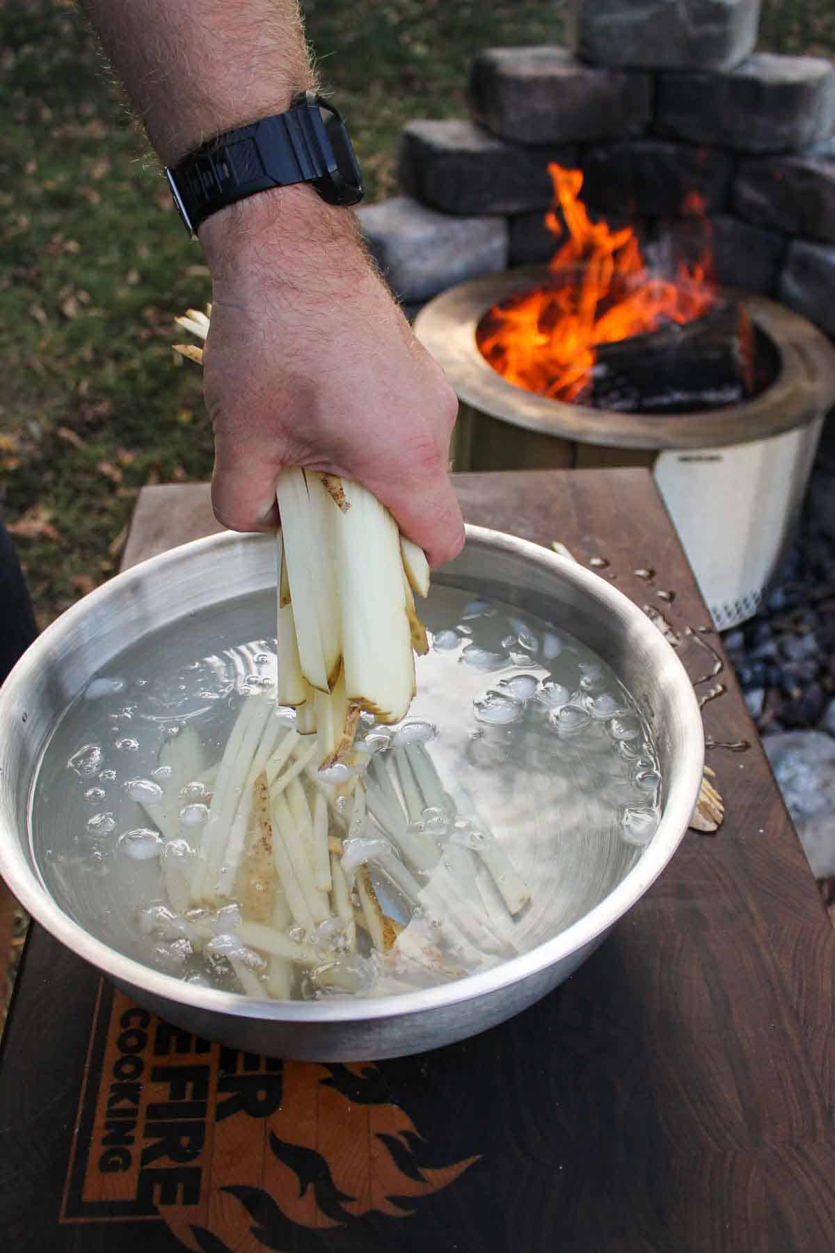 Placing raw fries into a bowl of ice water.