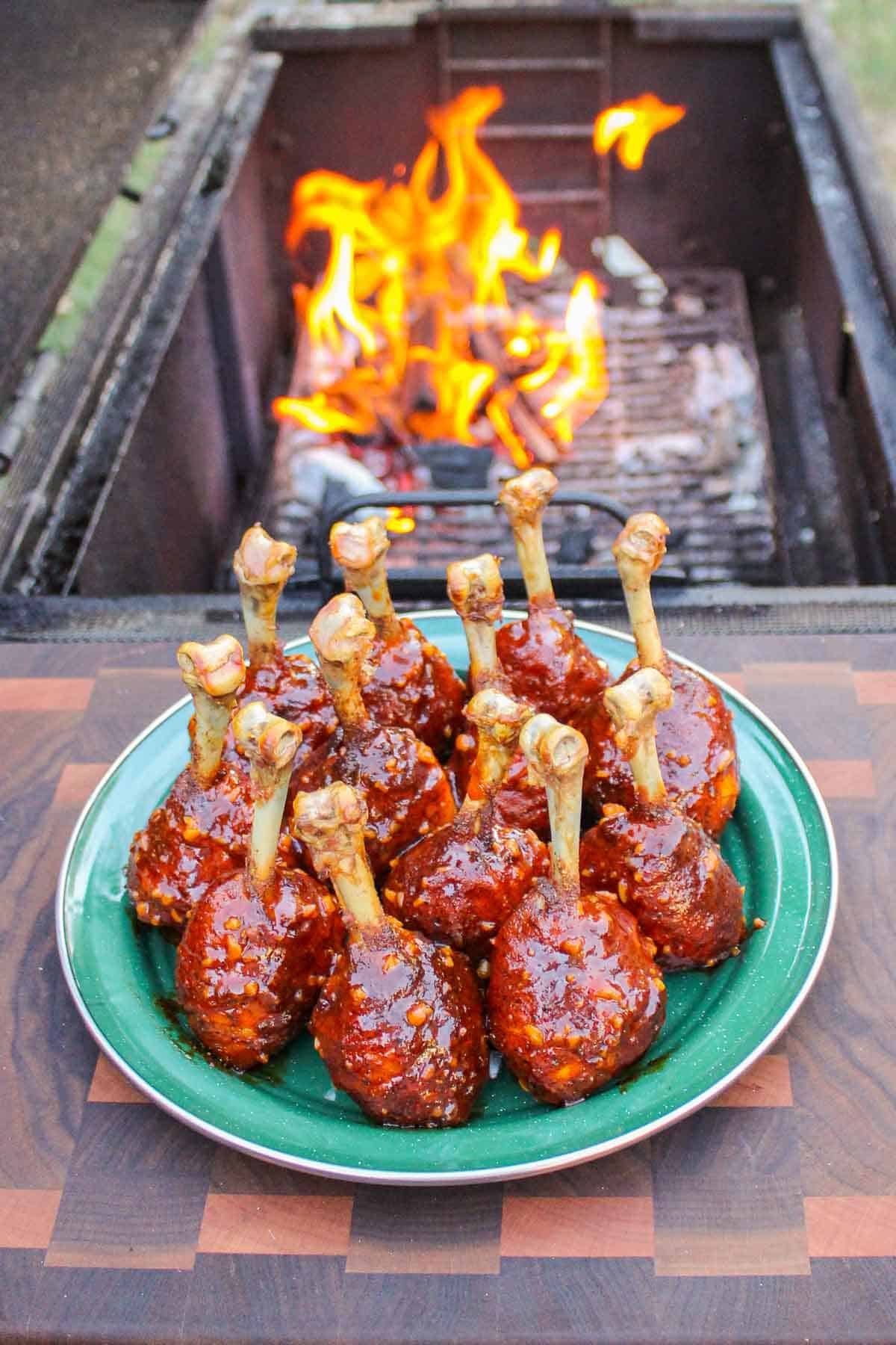 A plate full of chicken drumsticks with the fire's flames in the background.