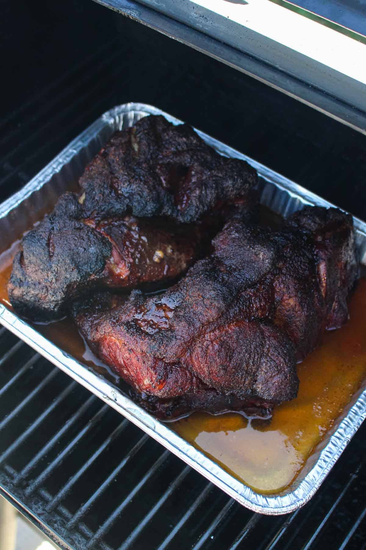 The pork butt being placed back on the grill, sitting in a tray with beef broth and light beer.