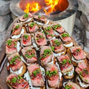 Grilled Steak Crostini assembled and sitting on a cutting board in front of the fire.