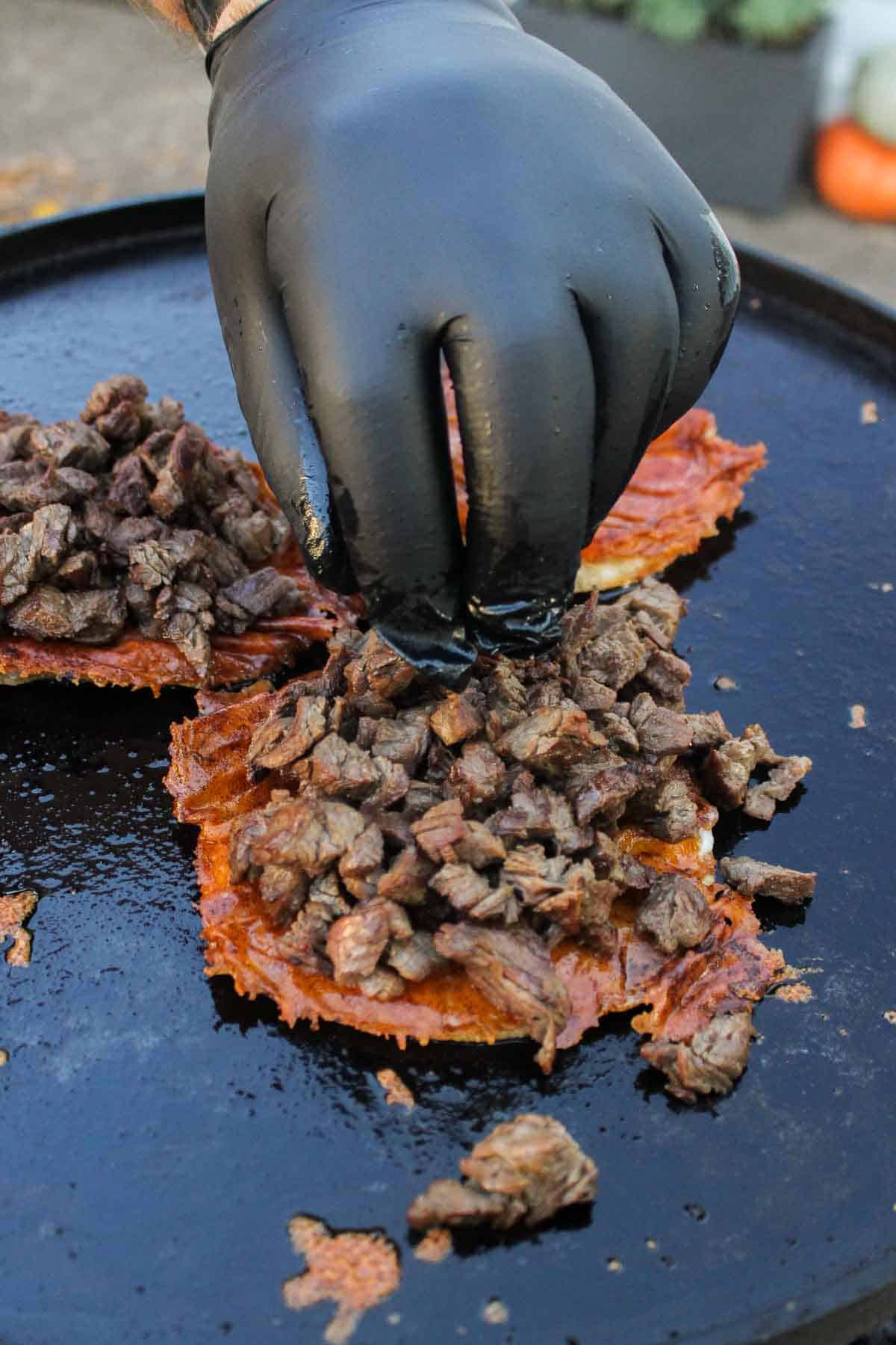 Placing the steak on top of the tortillas with melted cheese.