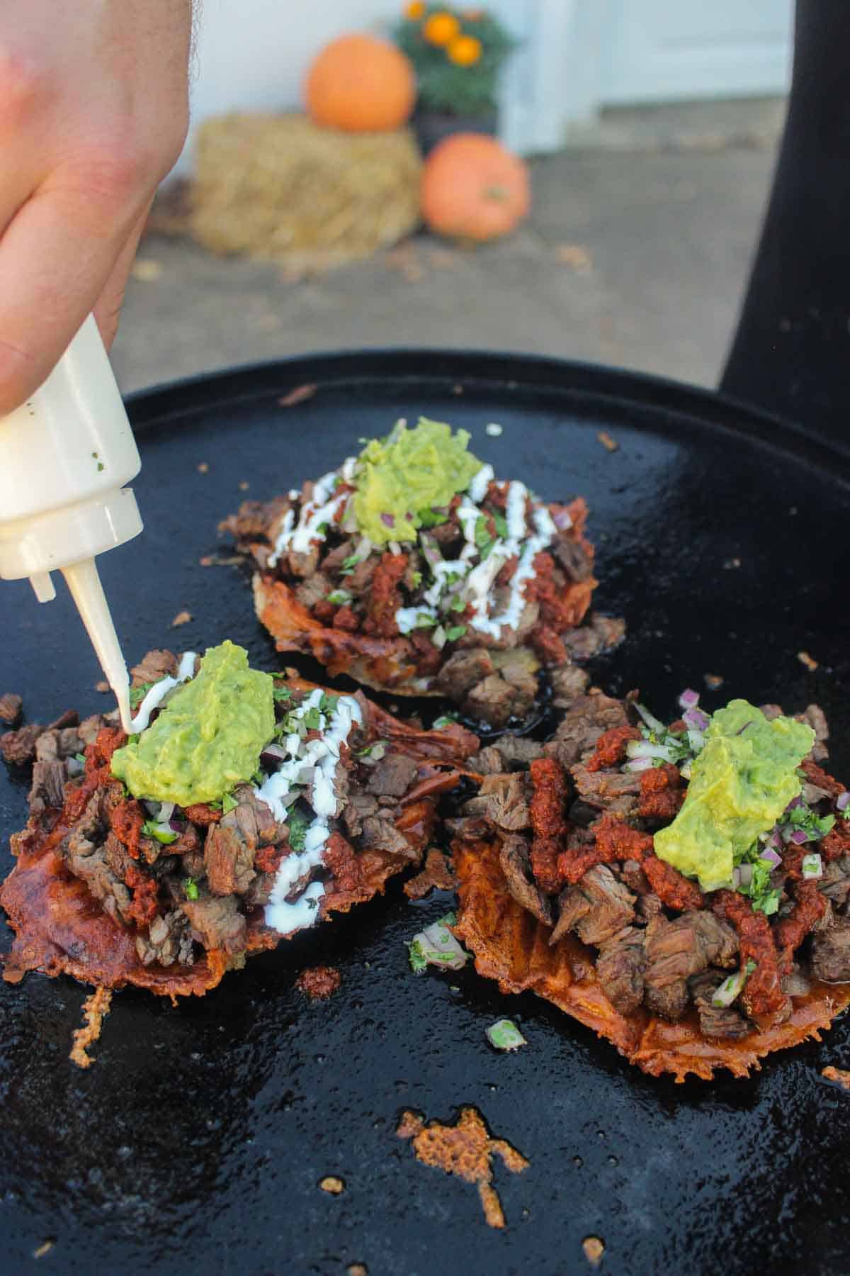 Topping the Grilled Steak Vampiro Tacos with Sour Cream.