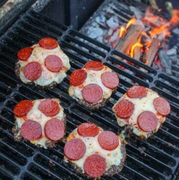 Smoked Pizza Burgers sitting on the grill with flames in the background.