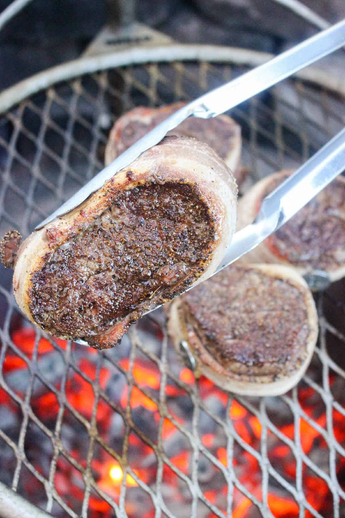 A close up of a grilled filet mignon being flipped.