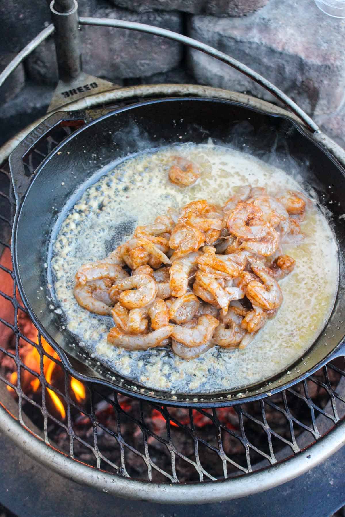 The shrimp cooking in the skillet with melted butter and minced garlic.