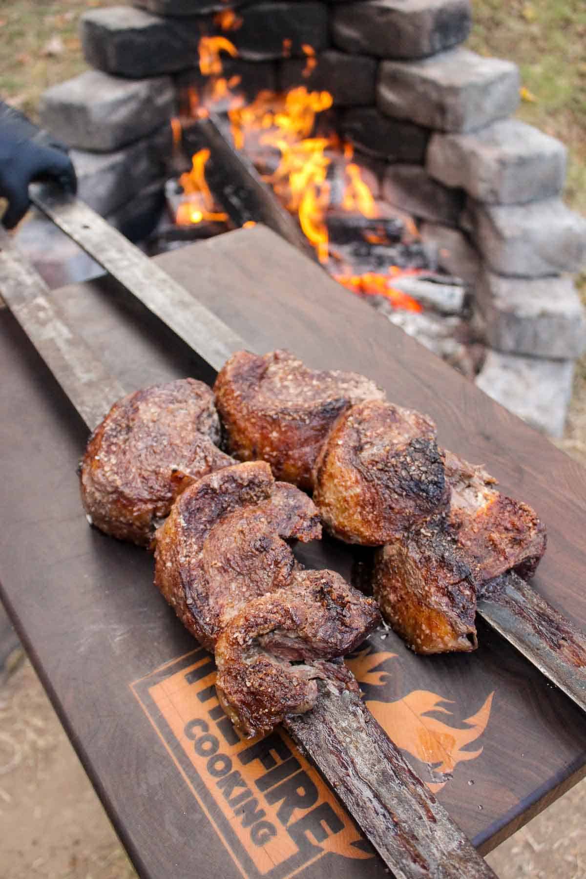 The cooked skewered picanha sitting on a cutting board after cooking.