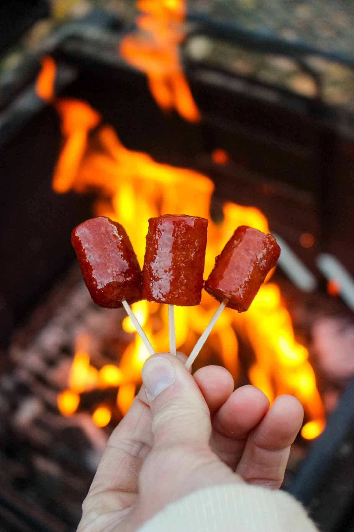Three Smoked Hot Dog Burnt Ends being held by the fire.
