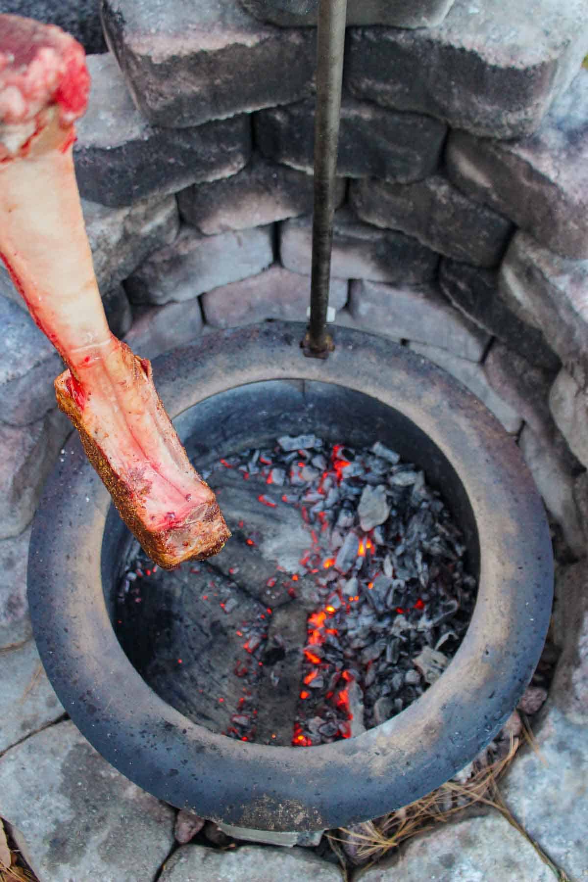 The tomahawk cooking indirectly by some burning embers.