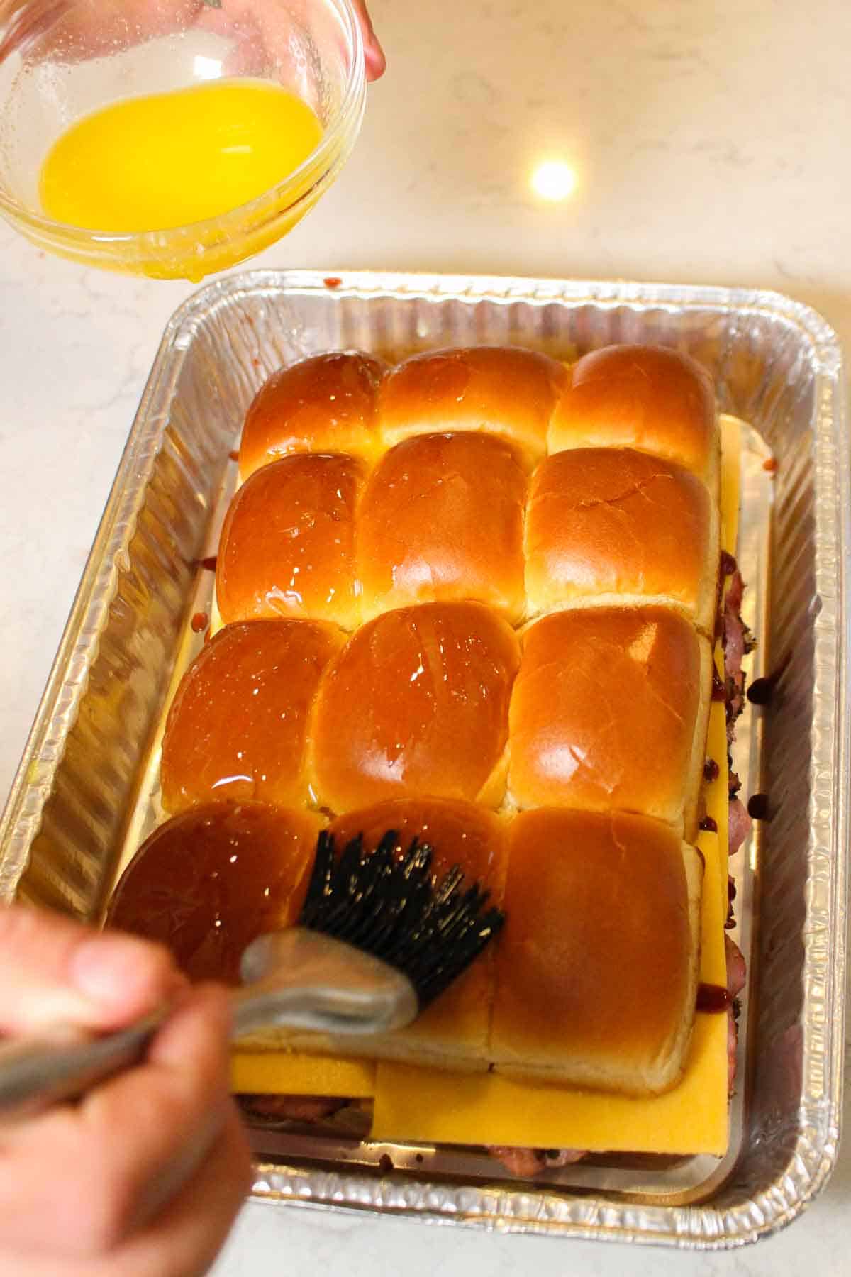 Adding butter to the top buns of the roast beef cheddar sliders. 