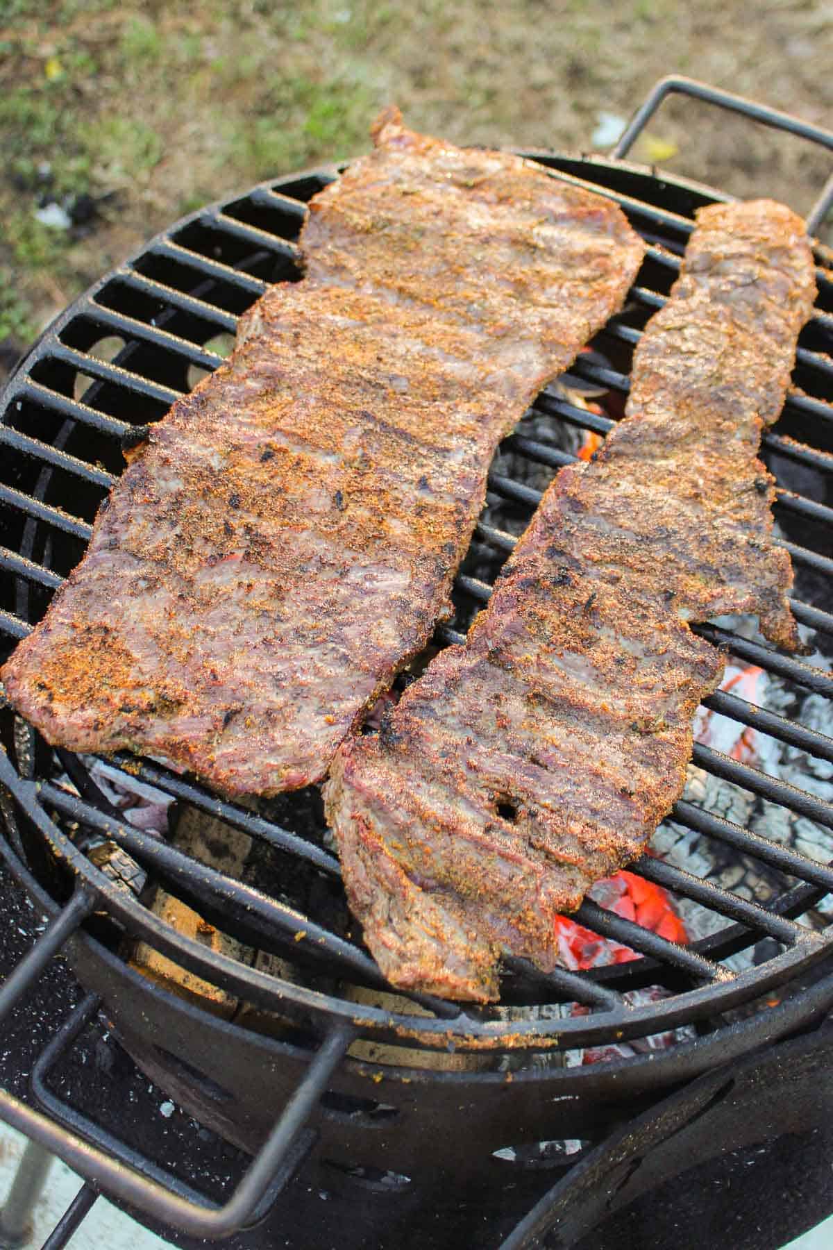 The two large skirt steaks cooking on the grill.