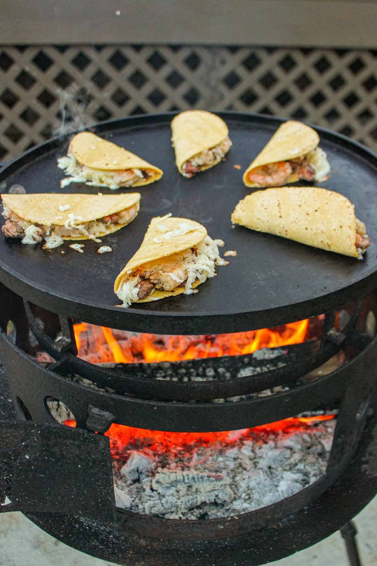 The crispy steak and shrimp tacos sitting assembled on the plancha over the fire.