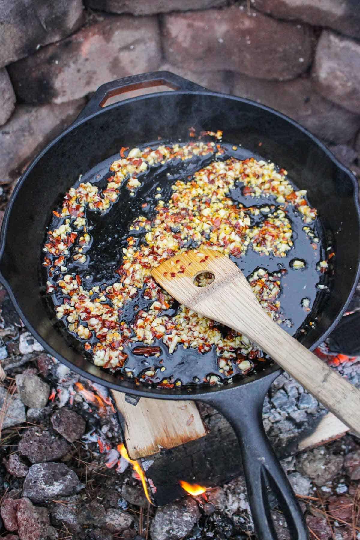 The garlic and red chili flakes browning in oil within the skillet.