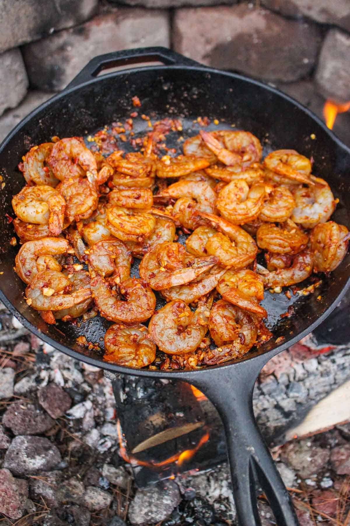 Adding the raw, seasoned shrimp to the skillet to cook.
