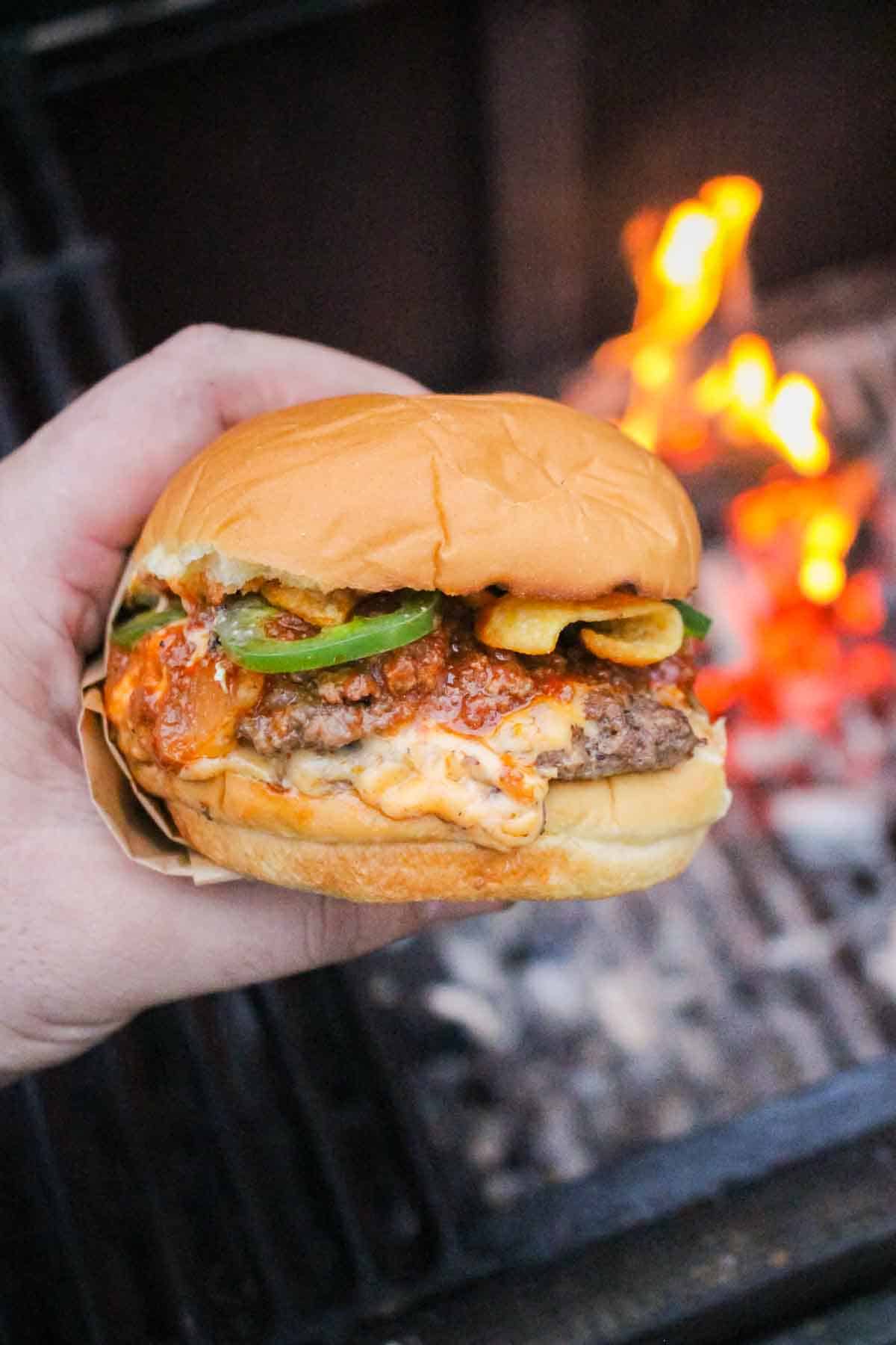One of the burgers being held with some flames in the background.