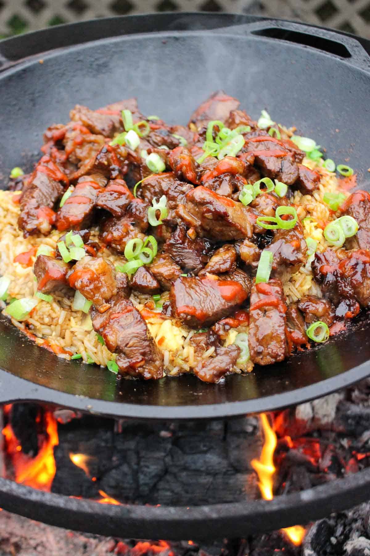 Garlic Teriyaki Steak Bites over a bed of fried rice sitting in the wok over the fire.