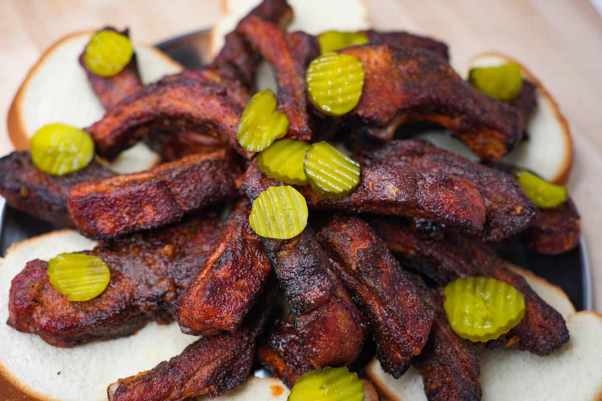 The Nashville Hot Smoke Fried Ribs sitting on white bread and garnished with pickle slices.