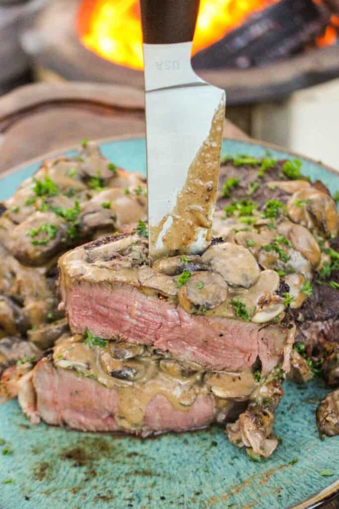 Bacon Wrapped Filet with Mushroom Cream Sauce sliced and sitting with a knife through the stack of steak.
