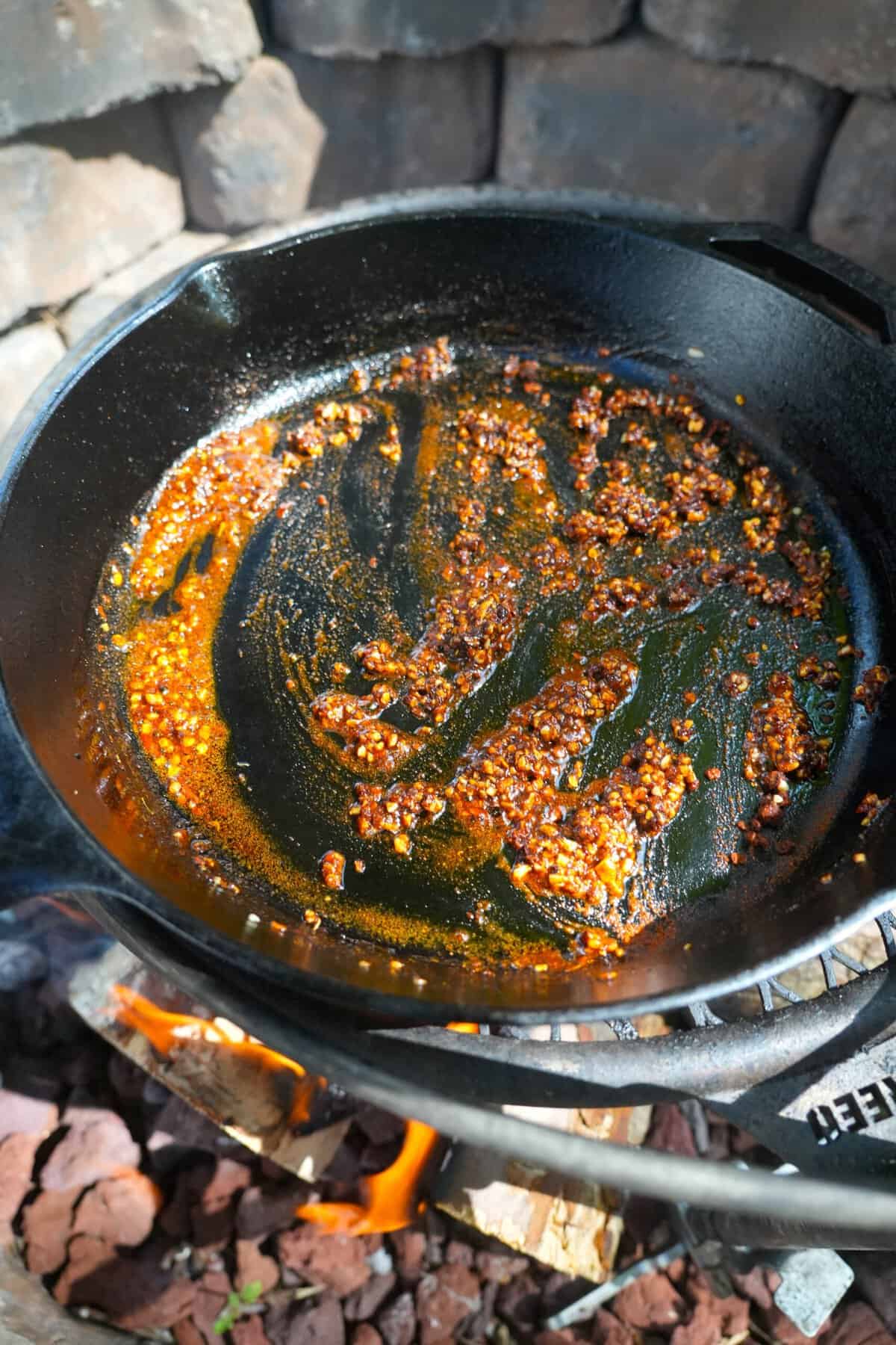 Adding seasonings like red pepper flakes and Cowboy Campfire Seasoning to a cast iron skillet