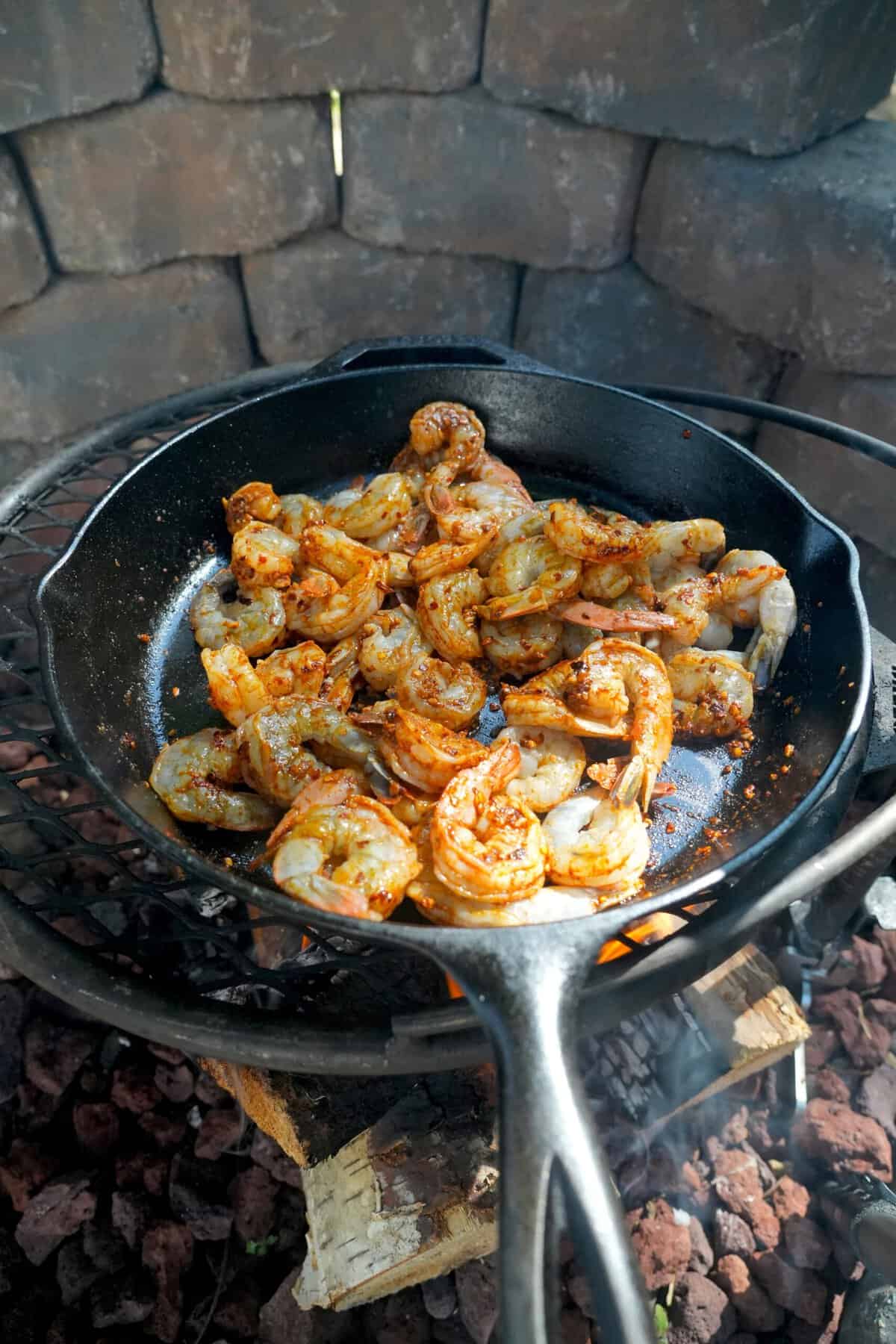 Adding peeled and deveined shrimp to a cast iron skillet over the grill to cook