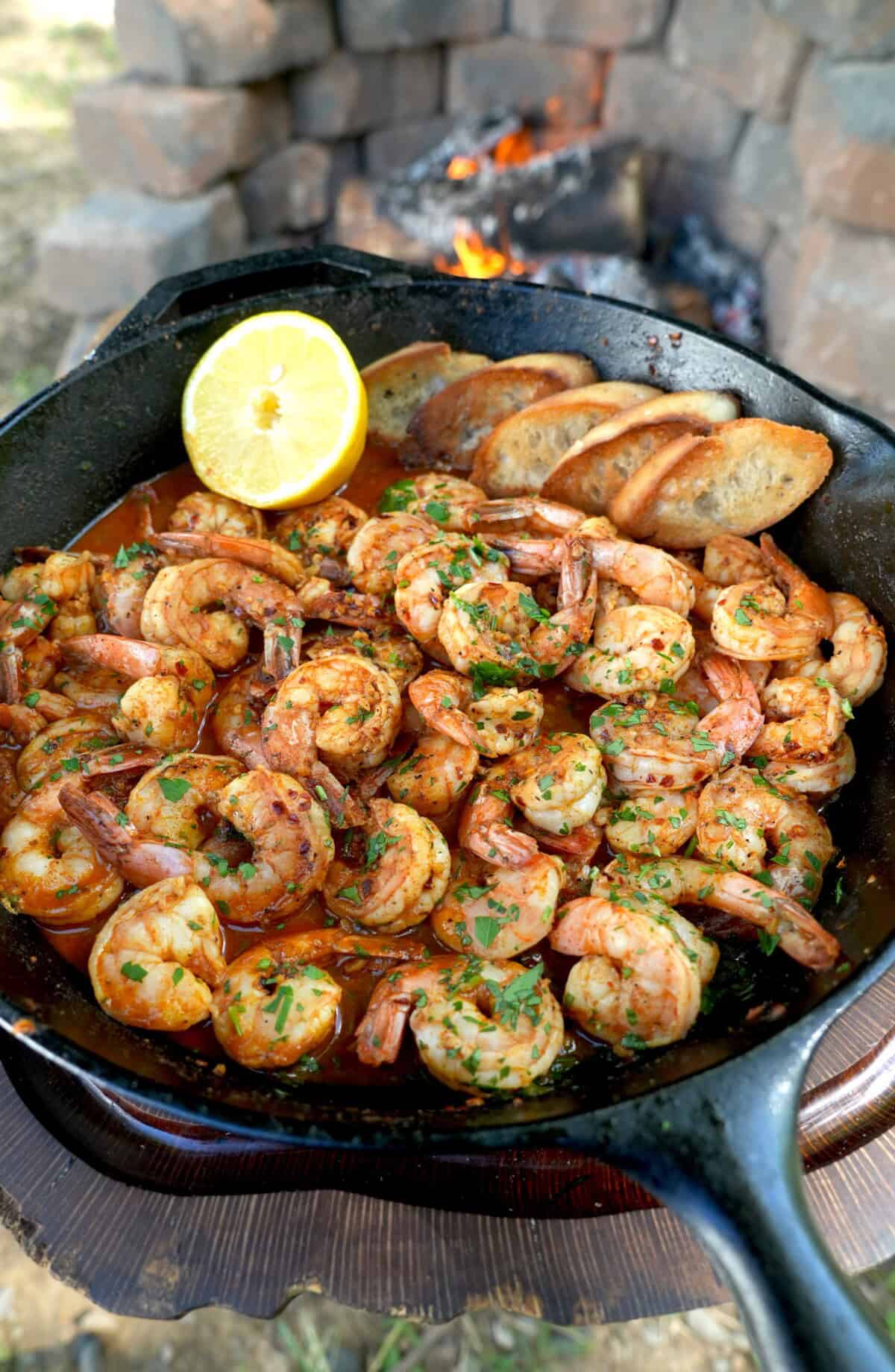 Cooked Spanish garlic shrimp in a skillet with a half lemon in the corner and chopped parsley as a garnish