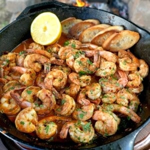 Cooked Spanish garlic shrimp in a skillet with a half lemon in the corner and chopped parsley as a garnish