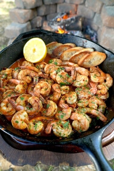 Cooked Spanish garlic shrimp in a skillet with a half lemon in the corner and chopped parsley as a garnish