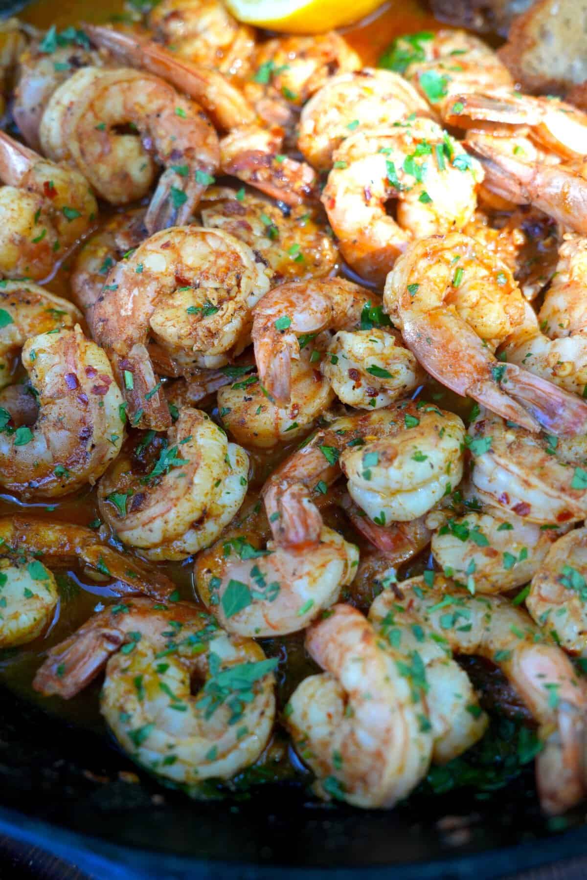 A close up of perfectly cooked Spanish garlic shrimp in a cast iron skillet and garnished with parsley