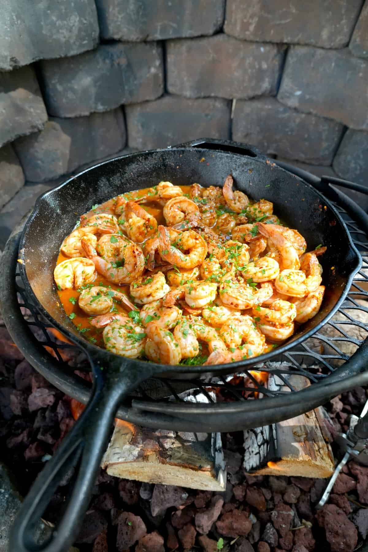 Cooking Spanish garlic shrimp in a cast iron skillet over the fire, surrounded by a stone pit