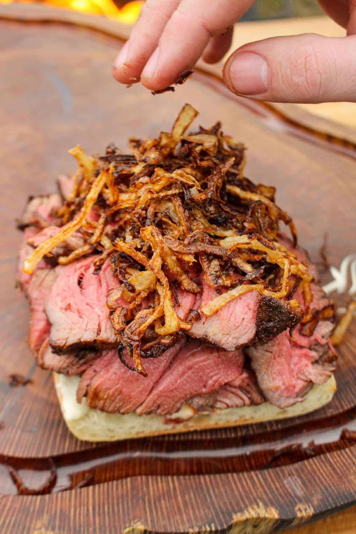 Placing the fried onions on the steak sandwich.