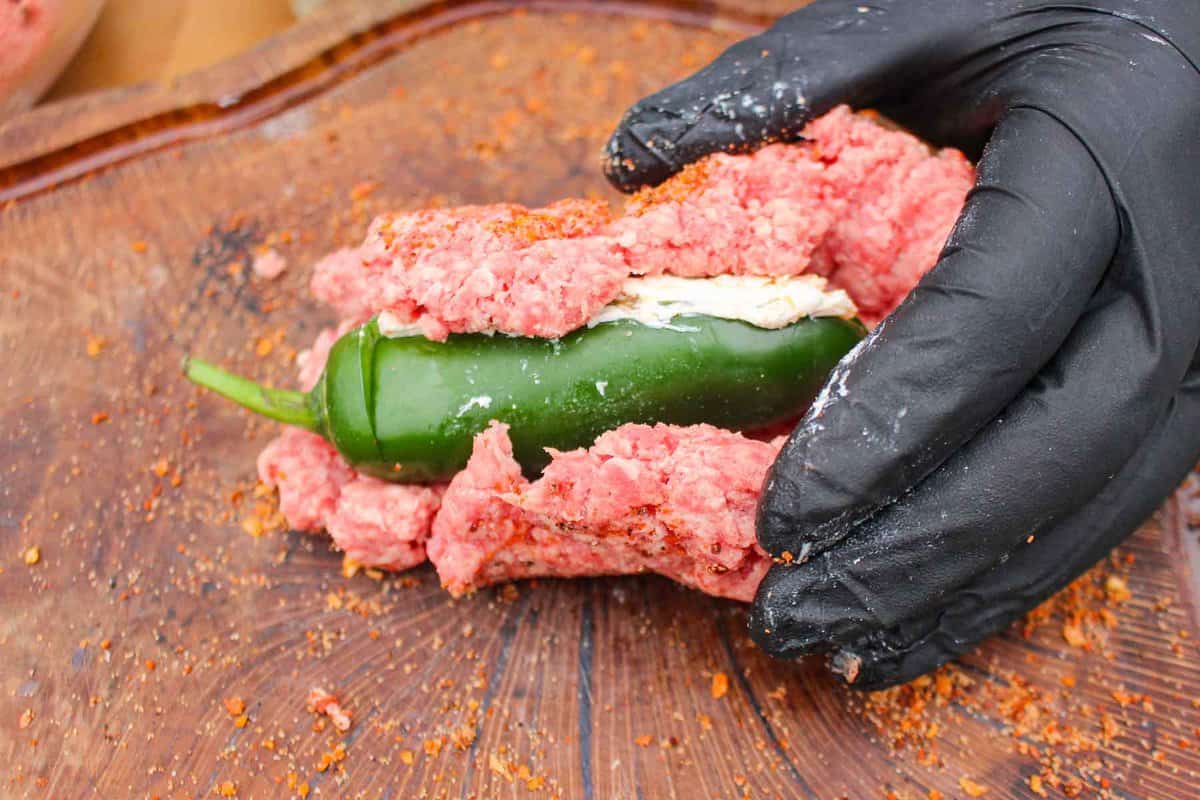 Wrapping the stuffed jalapeño in ground beef.