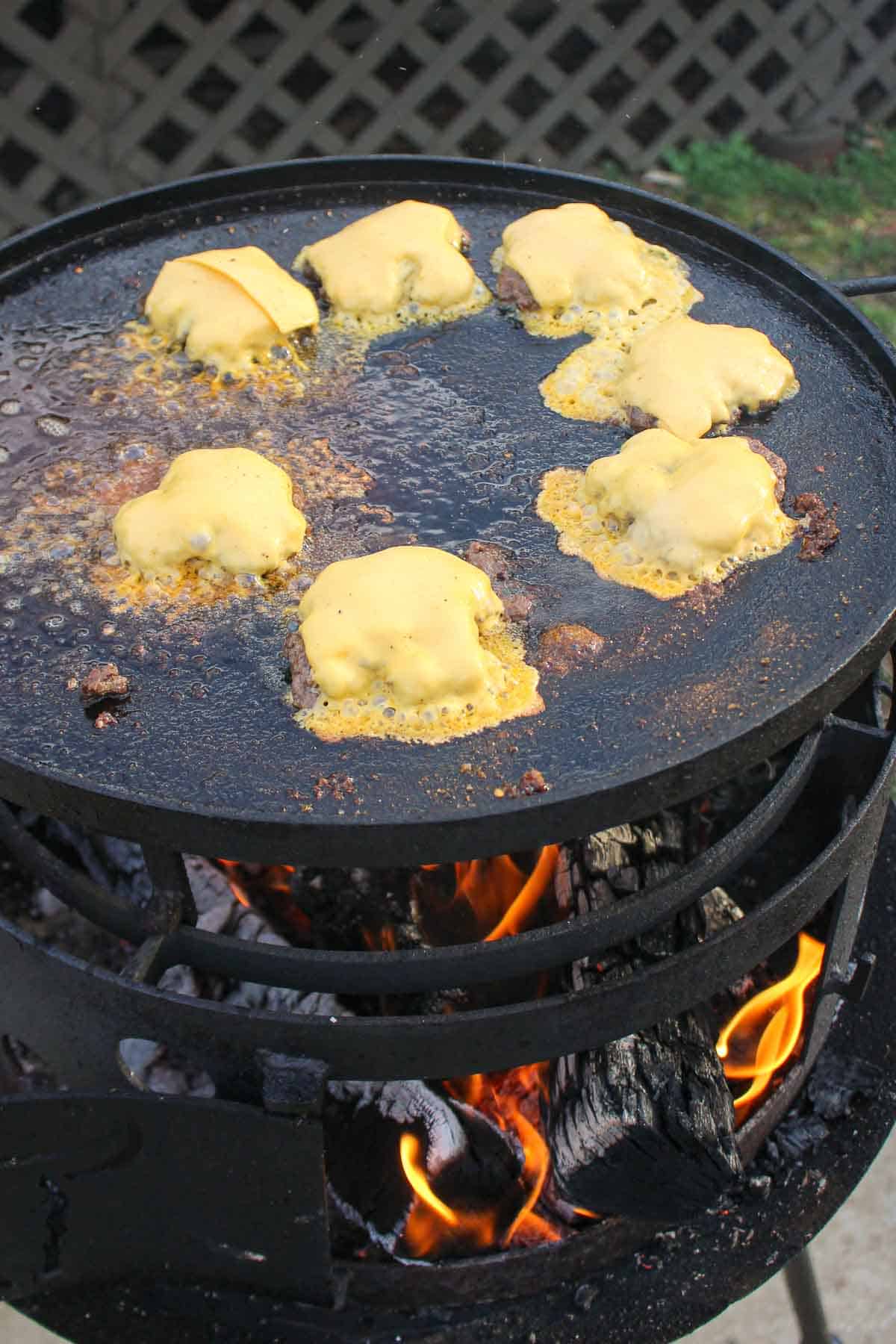 Melting cheese over the top of the  burger patties.