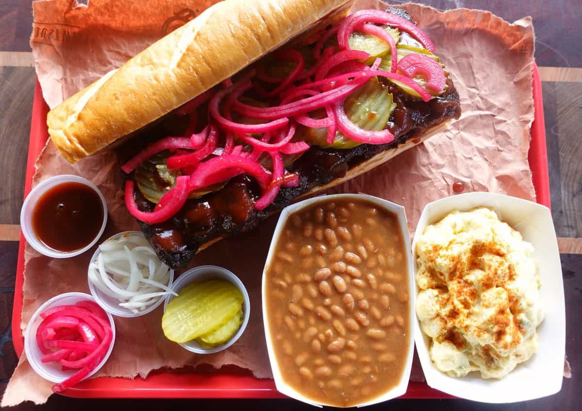 The assembled Beef McRib Sandwich complete with dill pickles and pickled onions with tasty baked beans and potato salad. 