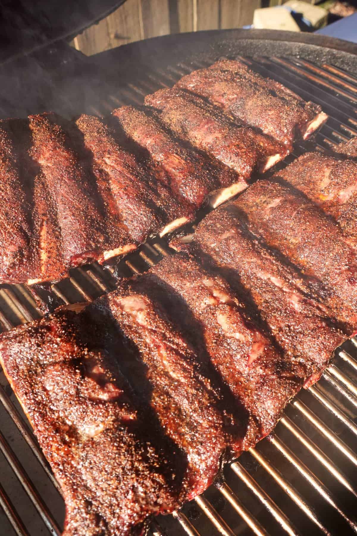 The beef ribs smoking on the grill.