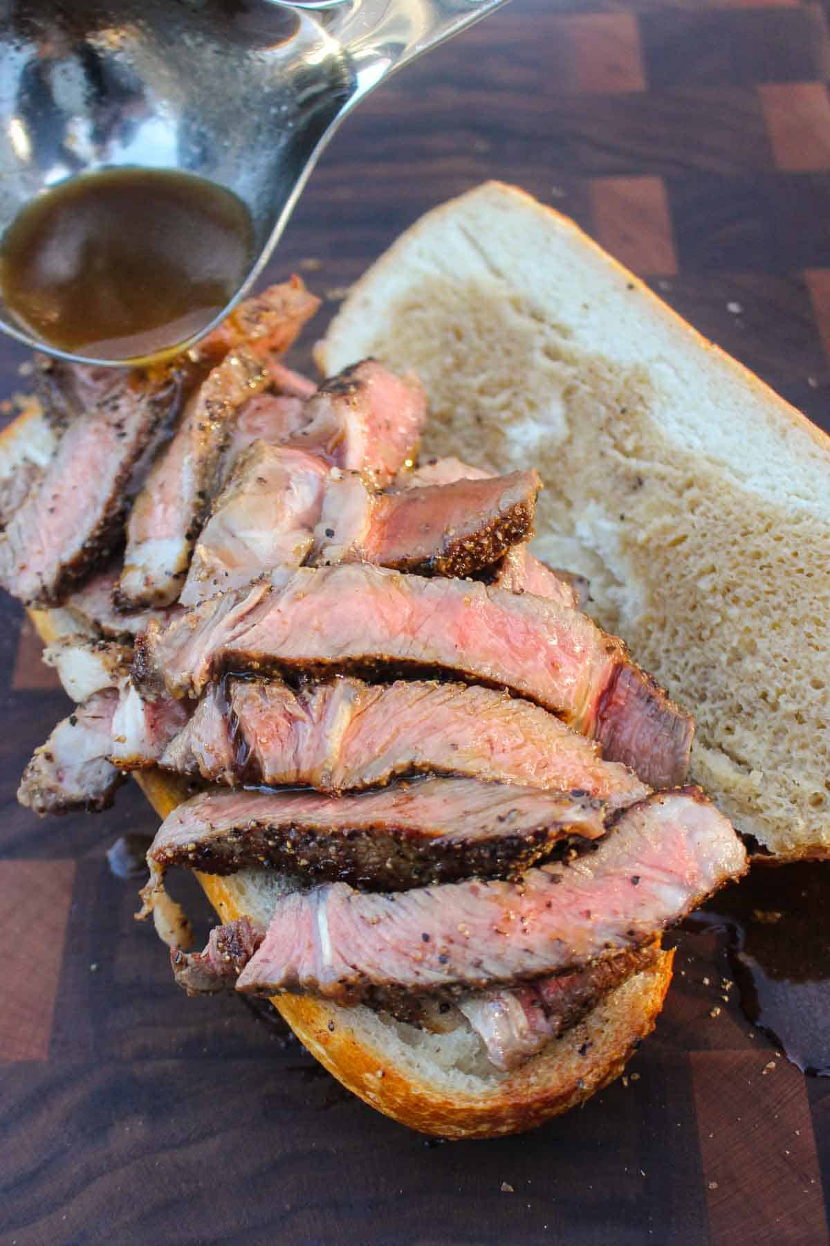 Adding the steak and au jus to the grilled French dip to form the sandwich.