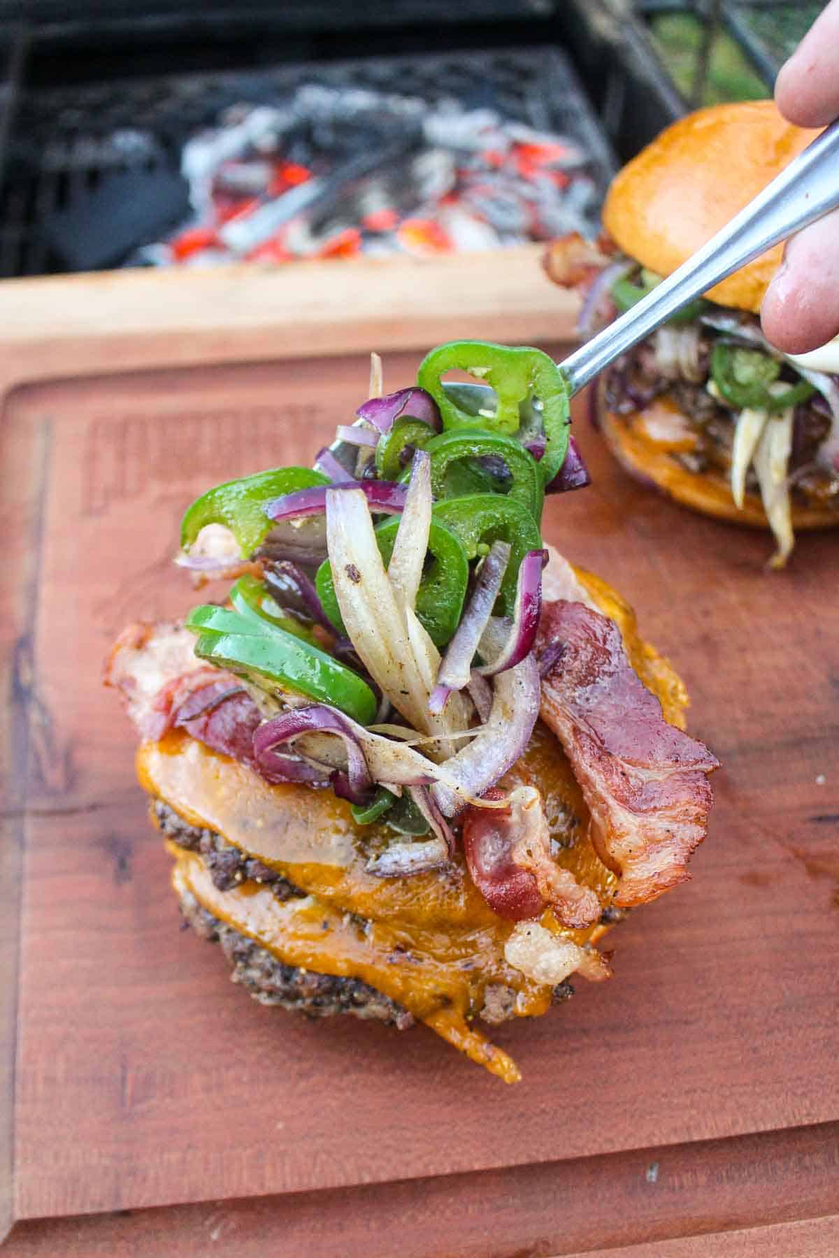 Placing the sautéed onions and jalapeños on top of a smash burger.