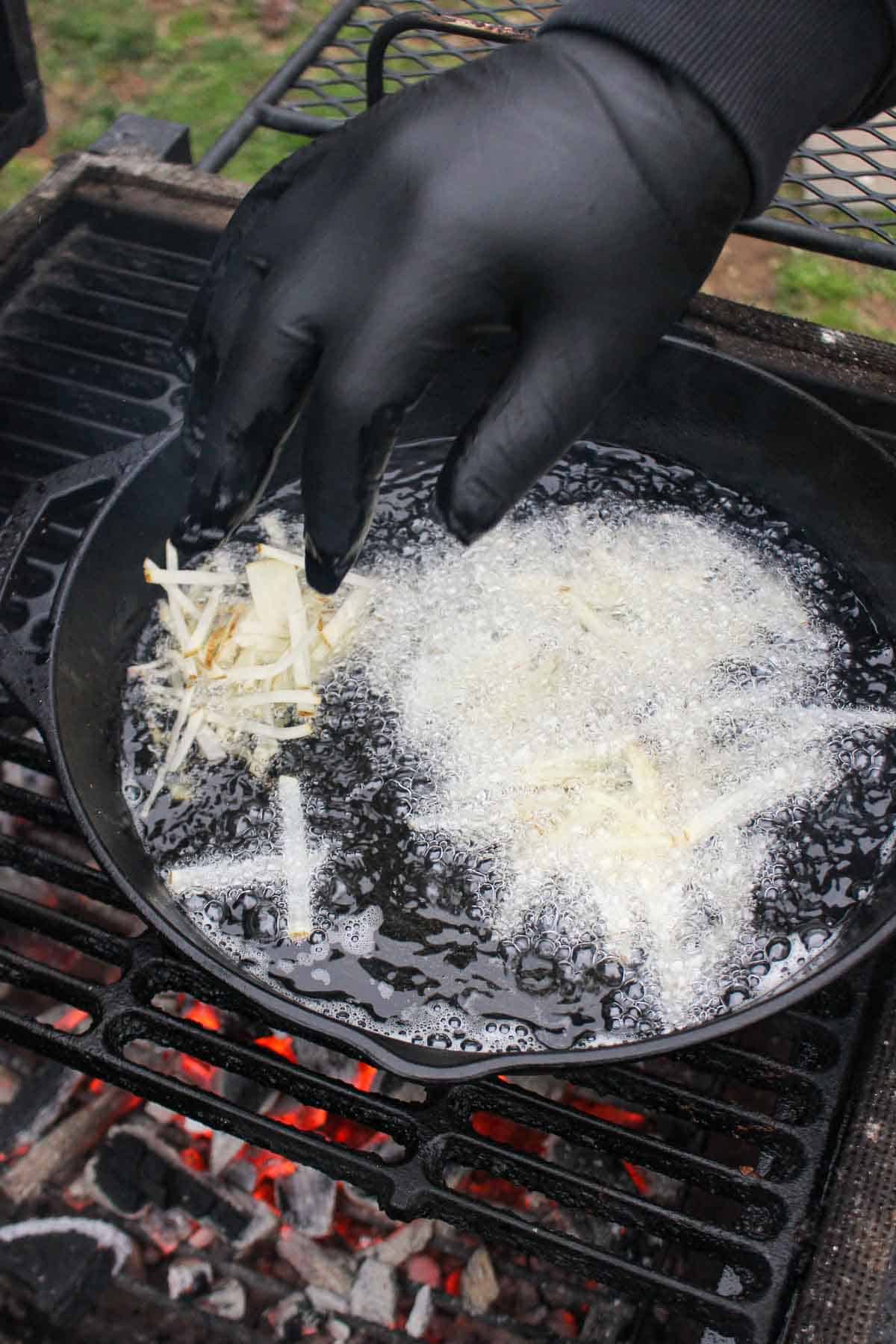Adding the thinly sliced potato fries into the hot oil so they can fry.