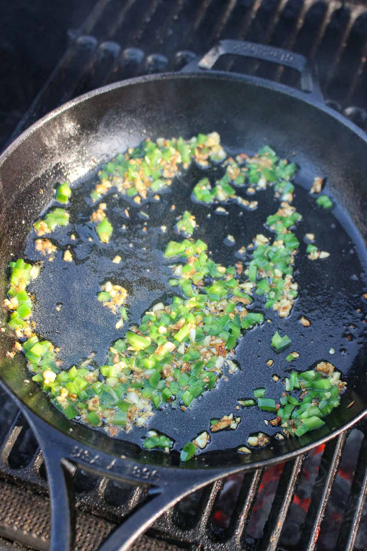 The sautéing of the jalapeños and garlic in a cast iron skillet.