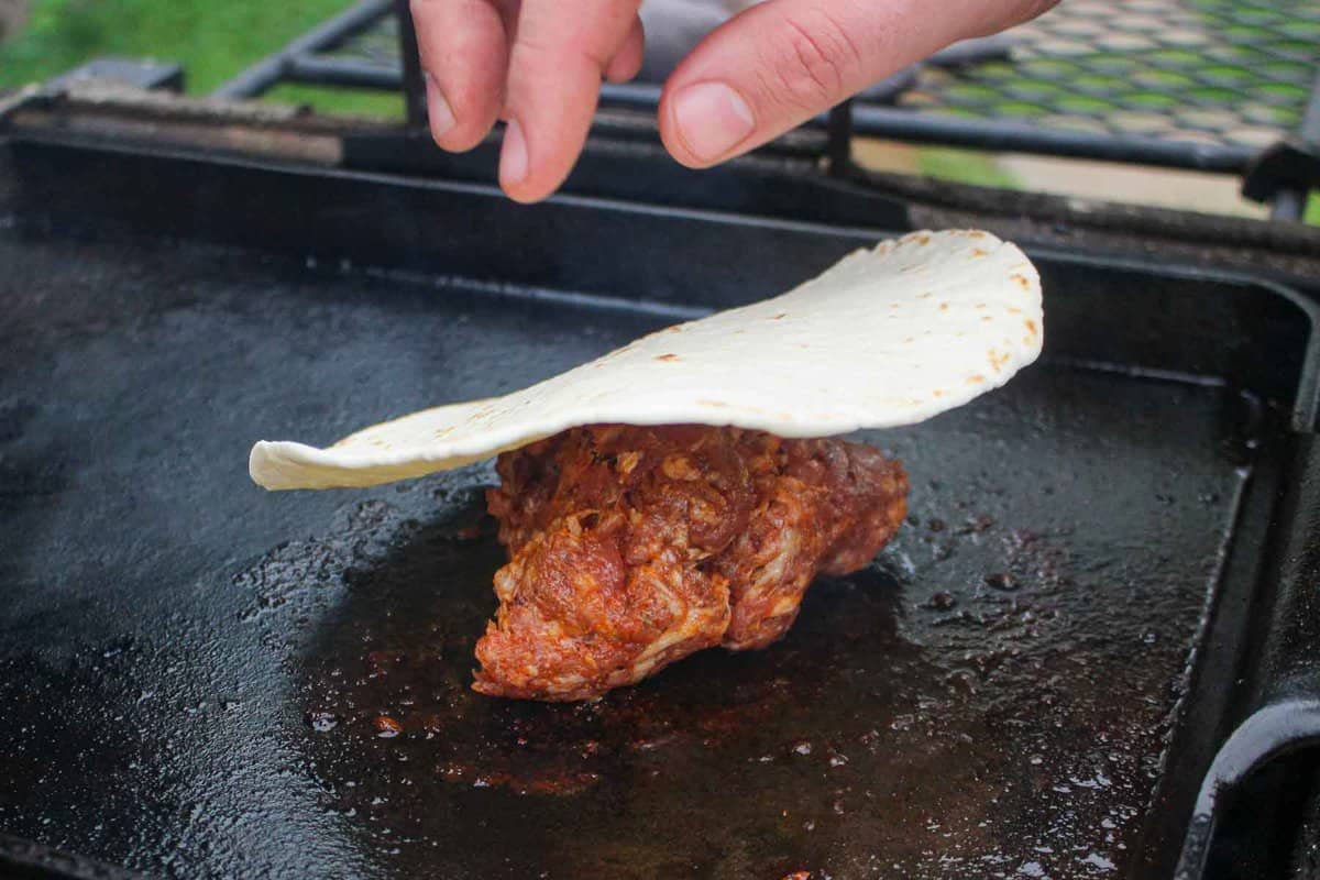 Adding a tortilla on top of a chorizo ball on the grill.