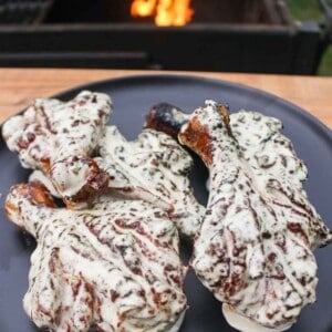 Butterflied Chicken Drumsticks with Jalapeño Lime White Sauce sitting on a serving plate in front of a fire.